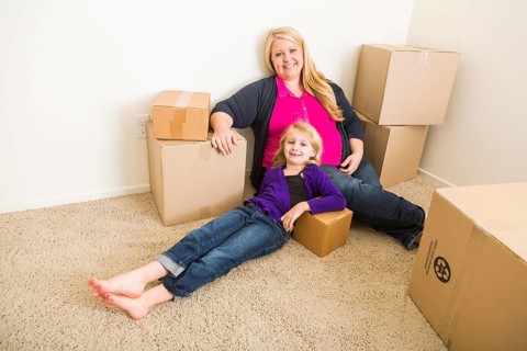 Happy young mother and daughter in empty room with moving boxes