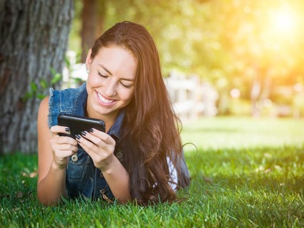 Attractive happy mixed-race young female laying in the grass texting on her cell phone outside
