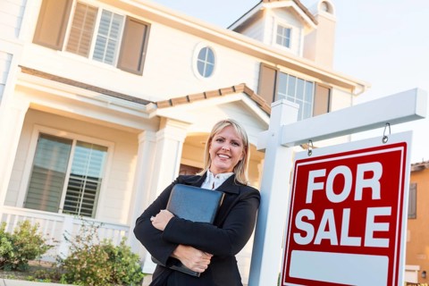 Female real estate agent in front of for sale sign and beautiful house