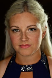 Portrait im Studio mit schwarzem Hintergrund von vorne einer jungen huebschen Frau mit langen blonden Haaren. Die Sommersprossen und die roten Lippen passen zu den blauen Augen