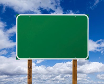 Blank green road sign with wooden posts over blue sky and clouds