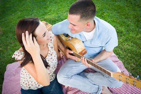 Young adult man playing guitar for his girlfriend in the park