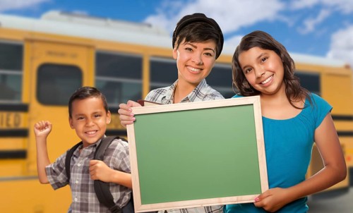 Young mixed-race students with blank chalkboard near school bus