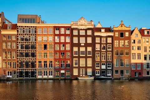 Houses and tourist boats on Amsterdam canal pier Damrak on sunset. Amsterdam