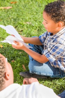 Happy african american father and mixed-race son playing with paper airplanes in the park