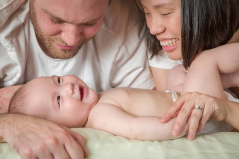 mixed-race chinese and caucasian baby boy laying in bed with his father and mother