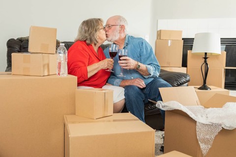 Senior adult couple toasting wine glasses surrounded by moving boxes