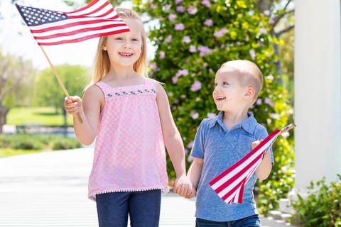 Young sister and brother waving american flags at the park