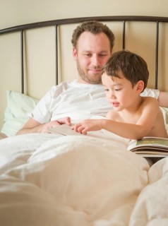 Chinese and caucasian baby boy reading a book in bed with his daddy