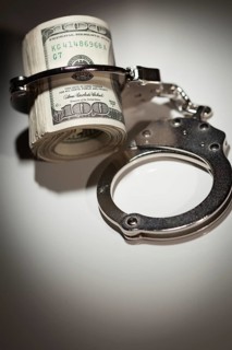 Handcuffs locked on roll of one hundred dollar bills under spotlight