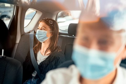A woman wearing a protective mask sitting on the back seat of a taxi car