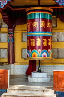 Buddhist monk rotating big prayer wheel with Om Mani Padme Hum Buddhist mantra prayer meaning Praise to the Jewel in the Lotus on kora around Tsuglagkhang complex. McLeod Ganj