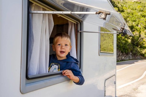 Happy small boy looking through the RV's window parked along the road