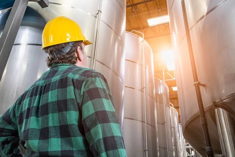 Man wearing hard hat looking up at large industrial tanks
