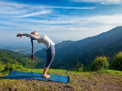 Young sporty fit man doing yoga Sun salutation Surya Namaskar pose Hasta Uttanasana outdoors in mountains
