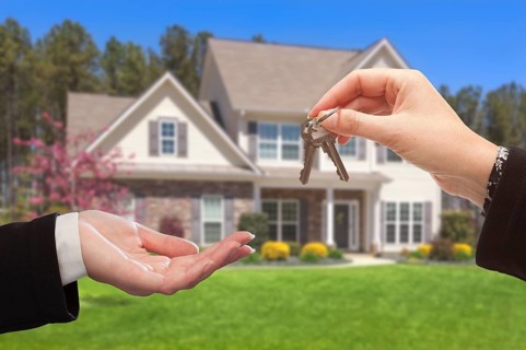 Real estate agent handing over the house keys in front of a beautiful new home