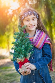 Cute mixed-race young girl holding small christmas tree outdoors