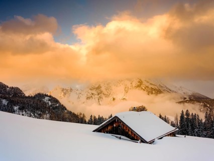 Snow-covered Priesbergalm in front of cloud-covered Watzmann
