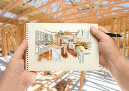 Male hands holding pen and pad of paper with custom kitchen illustration inside construction framing