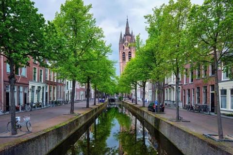Delt canal with old houses bicycles and cars parked along and Oude Kerk Old church tower
