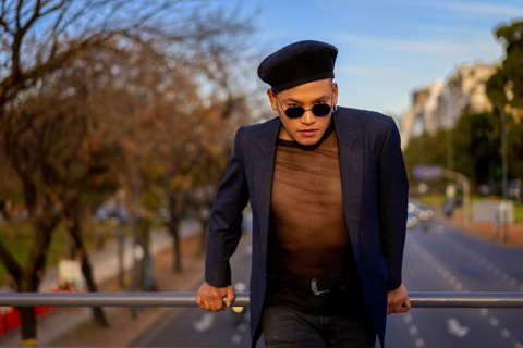 Latino gay male with makeup wearing trendy hat posing on a bridge