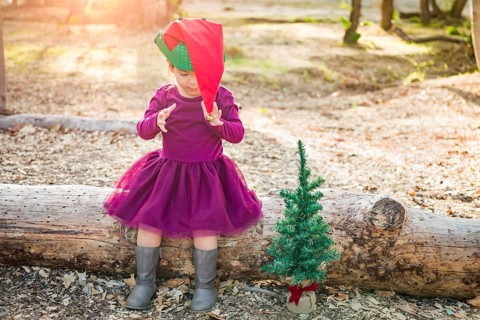 Cute mixed-race young baby girl having fun with christmas hat and tree outdoors