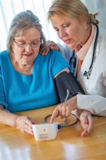 Senior adult woman learning from female doctor to use blood pressure machine