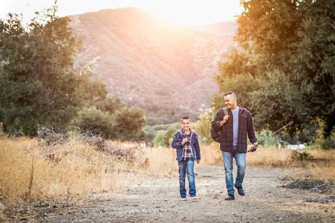 mixed-race father and son outdoors walking with fishing poles