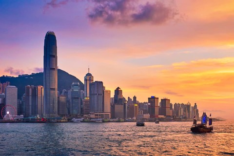 Hong Kong skyline cityscape downtown skyscrapers over Victoria Harbour in the evening with ferry boat and junk boat on sunset. Hong Kong