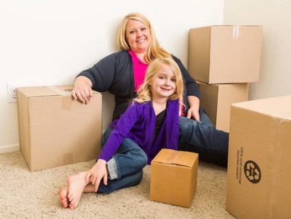 Happy young mother and daughter in empty room with moving boxes