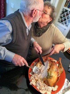 Senior adult couple cutting the holiday Turkey together in the kitchen