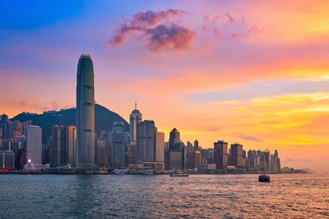 Hong Kong skyline cityscape downtown skyscrapers over Victoria Harbour in the evening with junk tourist ferry boat on sunset with dramatic sky. Hong Kong