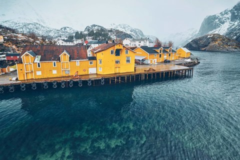Panorama of Nusfjord authentic fishing village with yellow rorbu houses in Norwegian fjord in winter. Lofoten islands