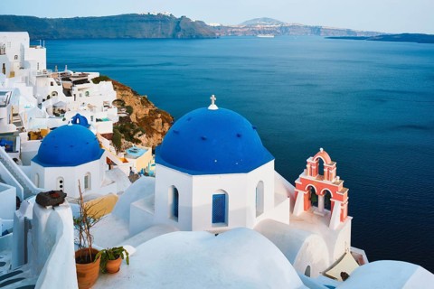Famous view from viewpoint of Santorini Oia village with blue dome of whitewashed greek orthodox Christian church of traditional greek architecture