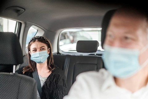 A woman wearing a protective mask sitting on the back seat of a taxi car