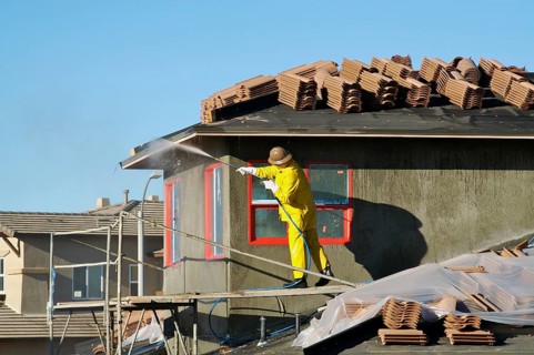 Construction worker pressure washes fresh applied surface of new home exterior