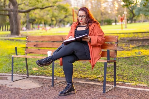 Woman sitting on a bench in a park checking her agenda and cell phone while having a coffee