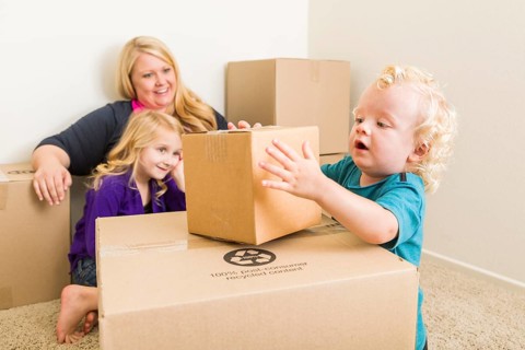 Playful young family in empty room playing with moving boxes