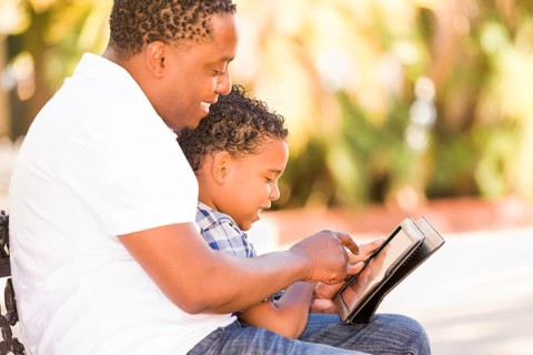 African american father and mixed-race son using computer tablet on bench in park