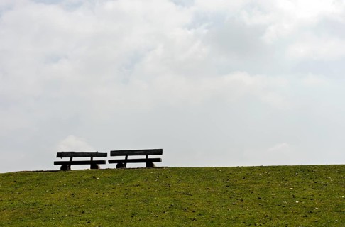 Zwei leere Baenke auf einer Deichkrone im Gegenlicht