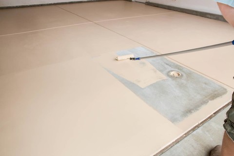 Worker painting floor of garage with roller
