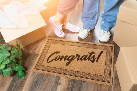 Man and woman unpacking near welcome mat with congrats