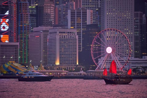 Tourist junk boat ferry with red sails and Hong Kong skyline cityscape downtown skyscrapers over Victoria Harbour in the evening. Hong Kong