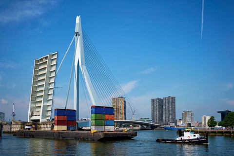 Tug boat towing barge with containers under open bascule part of Erasmusbrug bridge in Nieuwe Maas river. Rotterdam