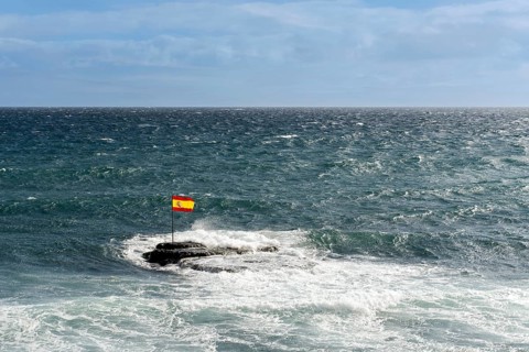 A Spanish flag on rocks in the Atlantic Ocean during windy weather in Pozo Izquierdo Bay