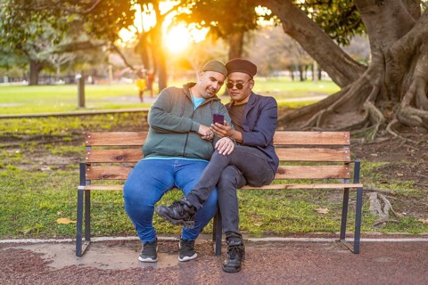 Gay Latino male couple sitting on a bench in a park at sunset