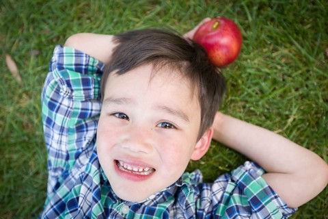 mixed-race chinese and caucasian young boy with apple relaxing on his back outside on the grass
