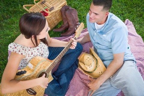 Young adult girl playing guitar with boyfriend in the park