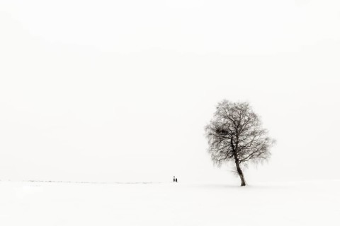 Einsame Frau knieend an Marterl mit Baum in Winterlandschaft