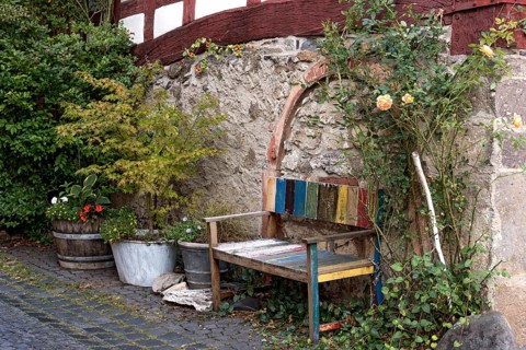 Old colourfully painted faded wooden bench and planter on house wall